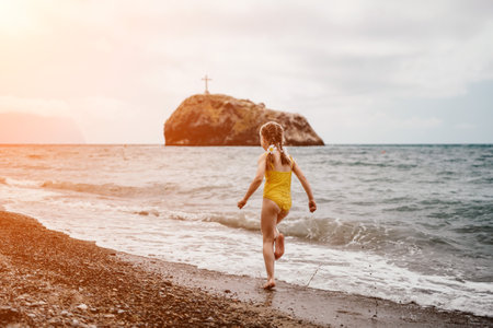 Cute little girl running along the seashore against a clear blue sea and rejoices in the rays of the summer sun. Beautiful girl in yellow swimsuit running and having fun on tropical beach.の写真素材
