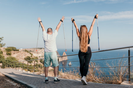 Happy Middle aged couple or friends practicing nordic walking in park near sea. Mature couple with trekking poles walking, practicing Nordic walking outdoors. Aging youthfully and sport conceptの写真素材