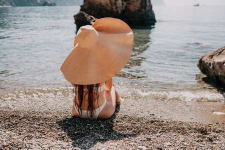 Woman travel sea. Happy tourist in hat enjoy taking picture outdoors for memories. Woman traveler posing on the beach at sea surrounded by volcanic mountains, sharing travel adventure journeyの写真素材