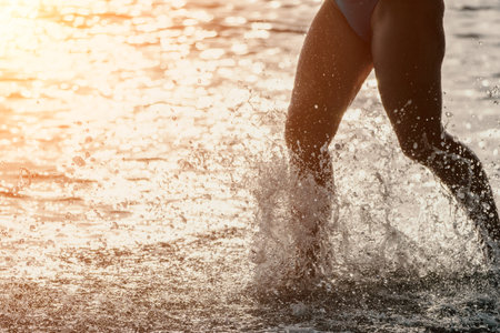 Running woman on a summer beach. A woman jogging on the beach at sunrise, with the soft light of the morning sun illuminating the sand and sea, evoking a sense of renewal, energy and health.の写真素材