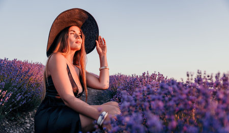 Woman lavender field. Happy carefree woman in black dress and hat with large brim walking in a lavender field during sunset. Perfect for inspirational and warm concepts in travel and wanderlust.の写真素材