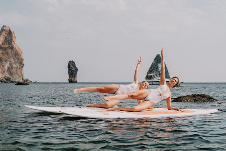 Woman sup yoga. Happy sporty woman practising yoga pilates on paddle sup surfboard. Female stretching doing workout on sea water. Modern individual female hipster outdoor summer sport activity.の写真素材