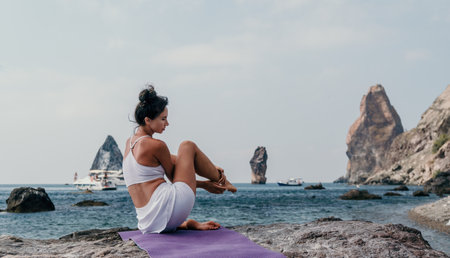 Fitness woman sea. A happy middle aged woman in white sportswear exercises morning outdoors on a beach with volcanic rocks by the sea. Female fitness pilates yoga routine concept. Healthy lifestyle.の写真素材