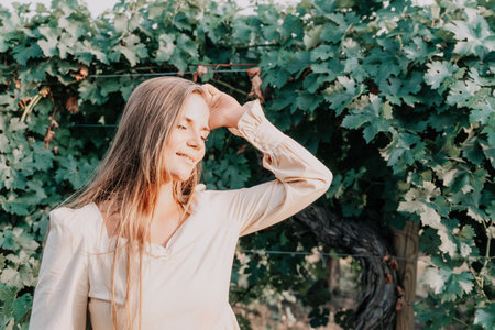 Woman at autumn winery. Portrait of happy woman holding glass of wine and enjoying in vineyard. Elegant young lady in hat toasting with wineglass smiling cheerfully enjoying her stay at vineyard.の写真素材