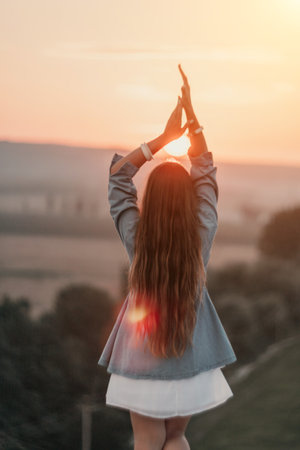 Happy woman standing with her back on the sunset in nature in summer with open hands. Romantic beautiful bride in white boho dress posing with mountains on sunsetの写真素材