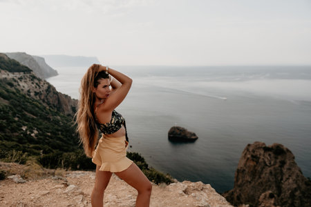 Woman travel sea. Happy tourist taking picture outdoors for memories. Woman traveler looks at the edge of the cliff on the sea bay of mountains, sharing travel adventure journeyの写真素材