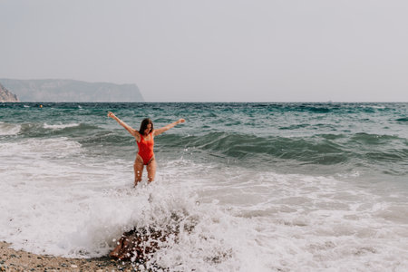 Woman summer travel sea. Happy tourist in red bikini enjoy taking picture outdoors for memories. Woman traveler posing on beach at sea surrounded by volcanic mountains, sharing travel adventure joyの写真素材