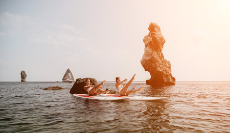 Woman sup yoga. Happy sporty woman practising yoga pilates on paddle sup surfboard. Female stretching doing workout on sea water. Modern individual female hipster outdoor summer sport activity.の写真素材