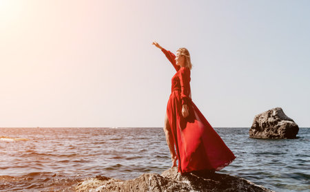 Woman travel sea. Happy tourist in long red dress enjoy taking picture outdoors for memories. Woman traveler posing on beach at sea surrounded by volcanic mountains, sharing travel adventure journeyの写真素材
