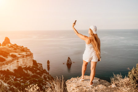 Woman travel sea. Happy tourist in hat enjoy taking picture outdoors for memories. Woman traveler posing on the beach at sea surrounded by volcanic mountains, sharing travel adventure journeyの写真素材