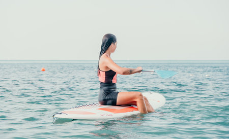 Sea woman sup. Silhouette of happy young woman in pink bikini, surfing on SUP board, confident paddling through water surface. Idyllic sunset. Active lifestyle at sea or riverの写真素材