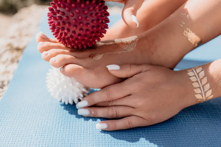 Woman sea pilates. Sporty happy middle aged woman practicing fitness on yoga mat with massage balls and roller near sea, smiling active female outside, enjoying healthy lifestyle, harmonyの写真素材