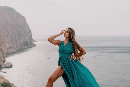 Woman travel portrait. Happy woman with long hair looking at camera and smiling. Close up portrait cute woman in a mint long dress posing on a volcanic rock high above the seaの写真素材