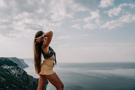 Woman travel sea. Happy tourist taking picture outdoors for memories. Woman traveler looks at the edge of the cliff on the sea bay of mountains, sharing travel adventure journeyの写真素材