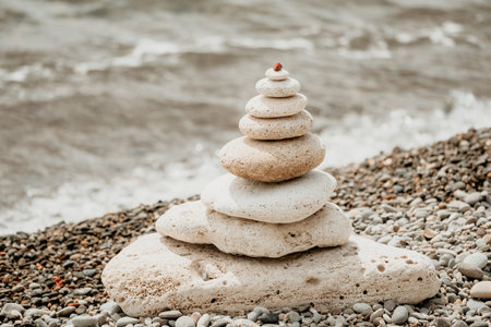 Balanced rock pyramid on sea pebbles beach, at sunset. Golden sea bokeh on background. Selective focus, zen stones on sea beach, meditation, spa, harmony, calm, balance conceptの写真素材