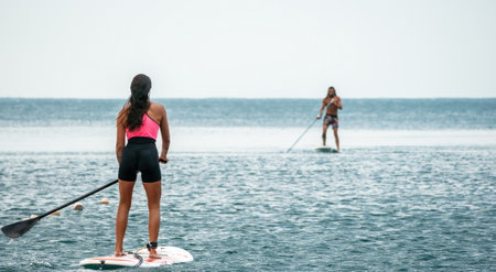 Sea woman and man on sup. Silhouette of happy young woman and man, surfing on SUP board, confident paddling through water surface. Idyllic sunset. Active lifestyle at sea or river.の写真素材