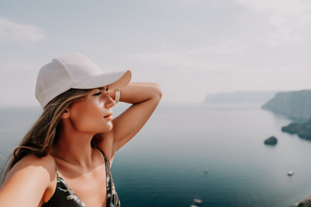 Woman travel sea. Happy tourist taking picture outdoors for memories. Woman traveler looks at the edge of the cliff on the sea bay of mountains, sharing travel adventure journeyの写真素材