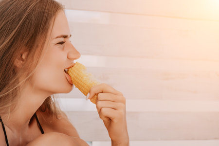 Woman eats corn on beach. Vegetarian hipster woman eat fresh organic grilled corn. Happy lady on sea beach sunset or ocean sunrise. Travel, explore, active yoga and meditation lifestyle concept.の写真素材
