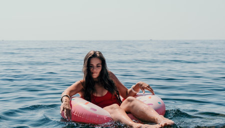 Woman summer sea. Happy woman swimming with inflatable donut on the beach in summer sunny day, surrounded by volcanic mountains. Summer vacation concept.の写真素材