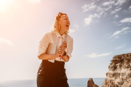 Digital nomad, Business woman working on laptop by the sea. Pretty lady typing on computer by the sea at sunset, makes a business transaction online from a distance. Freelance, remote work on vacationの写真素材