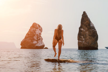 Woman sea yoga. Back view of free calm happy satisfied woman with long hair standing on top rock with yoga position against of sky by the sea. Healthy lifestyle outdoors in nature, fitness concept.の写真素材