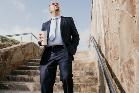 Confident middle age businessman with briefcase walking upstairs. Close-up of businessman wearing...