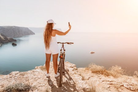 A woman cyclist on a mountain bike looking at the landscape of mountains and sea. Rear view of cyclist woman standing in front to the sea with outstretched arms. Freedom and healthy lifestyle concept.の写真素材
