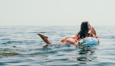 Woman summer sea. Happy woman swimming with inflatable donut on the beach in summer sunny day, surrounded by volcanic mountains. Summer vacation concept.の写真素材