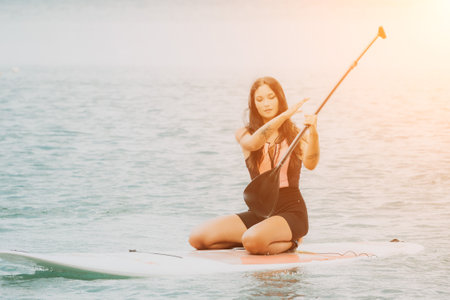 Close up shot of beautiful young caucasian woman with black hair and freckles looking at camera and smiling. Cute woman portrait in a pink bikini posing on sup board in the seaの写真素材