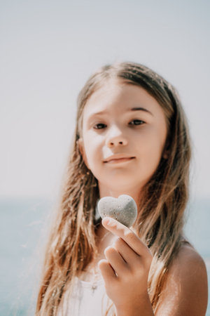 Happy Girl holding in hand a stone in the shape of a heart against the background of the sea. Summer vacation and travel concept. Happy holidays on ocean shoreの写真素材
