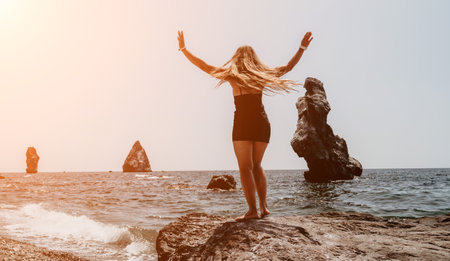 Woman summer travel sea. Happy tourist in hat enjoy taking picture outdoors for memories. Woman traveler posing on the beach at sea surrounded by volcanic mountains, sharing travel adventure journeyの写真素材