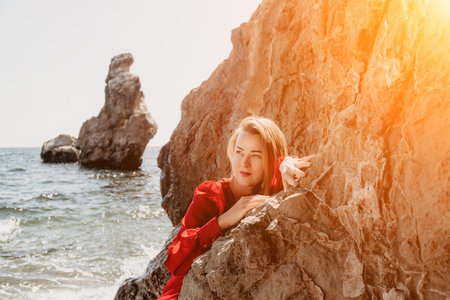 Woman travel sea. Happy tourist in long red dress enjoy taking picture outdoors for memories. Woman traveler posing on beach at sea surrounded by volcanic mountains, sharing travel adventure journeyの写真素材
