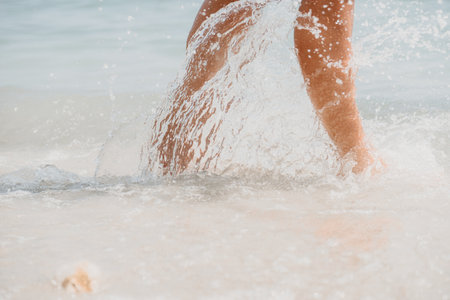Sea beach travel - woman walking on sand beach leaving footprints in the white sand. Female legs walking along the seaside barefoot, close-up of the tanned legs of a girl coming out of the water.の写真素材