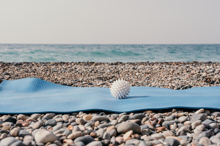 Blue yoga mat with white massage ball on a sandy pebble beach by the sea. Nobody. Womens yoga fitness routine. Healthy lifestyle, harmonyの写真素材
