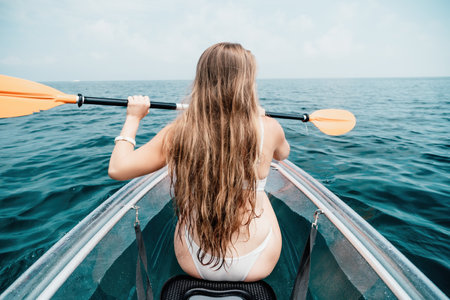 Woman in kayak back view. Happy young woman with long hair floating in transparent kayak on the crystal clear sea. Summer holiday vacation and cheerful female people relaxing having fun on the boatの写真素材