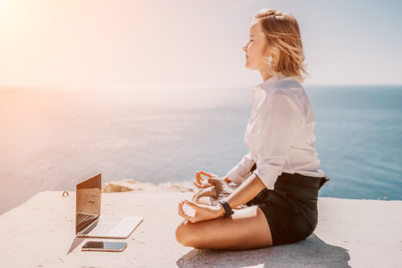 Woman sea laptop yoga. Business woman freelancer in yoga pose working over blue sea beach at laptop and meditates. Girl relieves stress from work. Freelance, digital nomad, travel and holidays conceptの写真素材