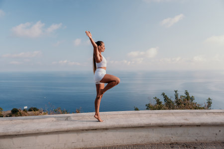 Fitness woman sea. A happy middle aged woman in white sportswear exercises morning outdoors in a park with a beach view. Female fitness pilates yoga routine concept. Healthy lifestyle.の写真素材