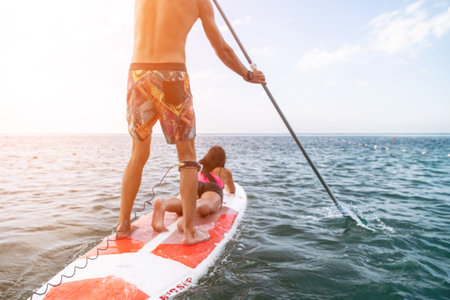Sea woman and man on sup. Silhouette of happy young woman and man, surfing on SUP board, confident paddling through water surface. Idyllic sunset. Active lifestyle at sea or river.の写真素材