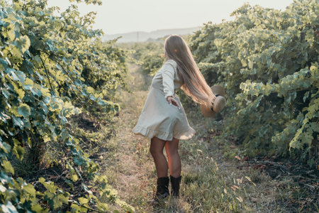Woman at autumn winery. Portrait of happy woman holding glass of wine and enjoying in vineyard. Elegant young lady in hat toasting with wineglass smiling cheerfully enjoying her stay at vineyard.の写真素材