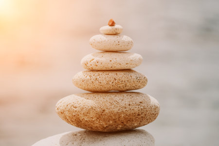 Pyramid stones on seashore with warm sunset on sea background for perfect holiday. Pebble beach and calm sea create a serene travel destination. concepts of happy vacation, meditation spa and calmnessの写真素材