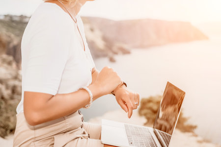 Digital nomad, Business woman working on laptop by the sea. Pretty lady typing on computer by the sea at sunset, makes a business transaction online from a distance. Freelance, remote work on vacationの写真素材