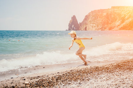 Cute little girl running along the seashore against a clear blue sea and rejoices in the rays of the summer sun. Beautiful girl in yellow swimsuit running and having fun on tropical beach.の写真素材