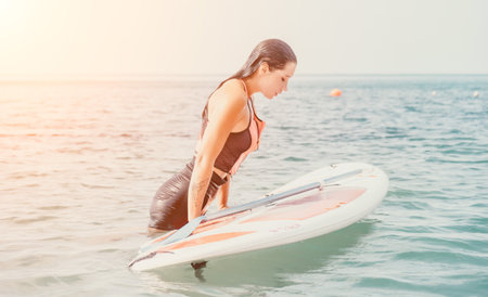 Sea woman sup. Silhouette of happy young woman in pink bikini, surfing on SUP board, confident paddling through water surface. Idyllic sunset. Active lifestyle at sea or river.の写真素材