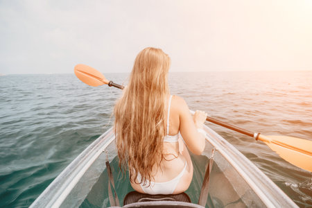 Woman in kayak back view. Happy young woman with long hair floating in transparent kayak on the crystal clear sea. Summer holiday vacation and cheerful female people relaxing having fun on the boatの写真素材