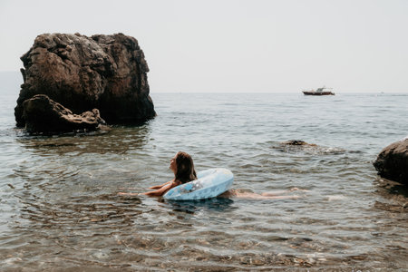 Woman summer sea. Happy woman swimming with inflatable donut on the beach in summer sunny day, surrounded by volcanic mountains. Summer vacation concept.の写真素材