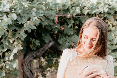 Woman at autumn winery. Portrait of happy woman holding glass of wine and enjoying in vineyard. Elegant young lady in hat toasting with wineglass smiling cheerfully enjoying her stay at vineyard.の写真素材