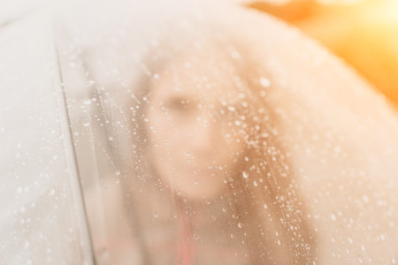 Woman rain umbrella. Happy woman portrait wearing a raincoat with transparent umbrella outdoors on rainy day in park near sea. Girl on the nature on rainy overcast day.の写真素材