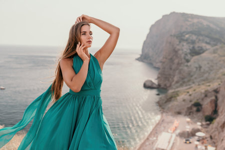 Woman travel portrait. Happy woman with long hair looking at camera and smiling. Close up portrait cute woman in a mint long dress posing on a volcanic rock high above the seaの写真素材