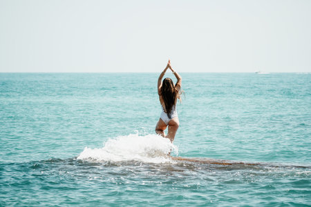 Woman sea yoga. Back view of free calm happy satisfied woman with long hair standing on top rock with yoga position against of sky by the sea. Healthy lifestyle outdoors in nature, fitness conceptの写真素材