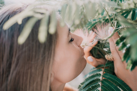 Beauty portrait of happy woman closeup. Young girl smelling Chinese acacia pink blossoming flowers....